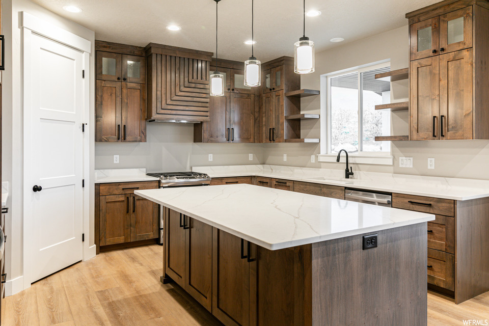 Kitchen with custom range hood, a center island, light stone counters, decorative light fixtures, and light hardwood / wood-style flooring