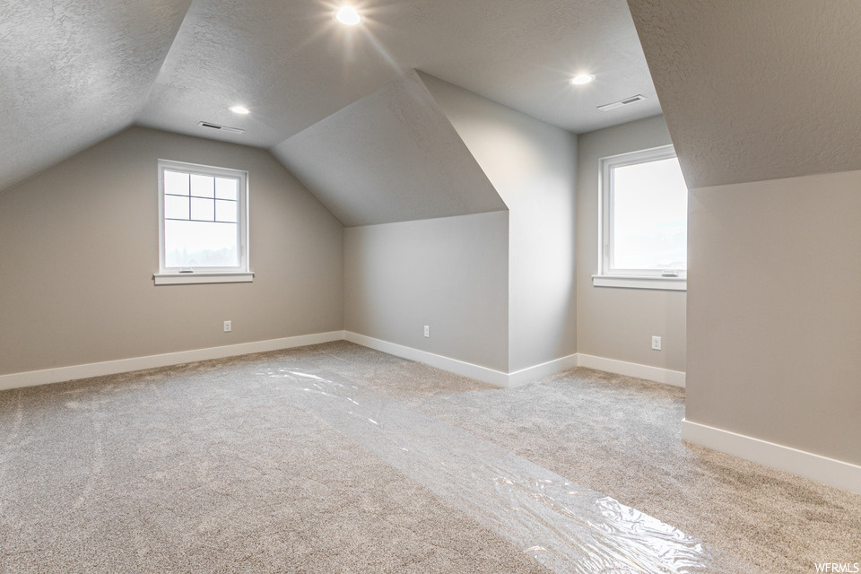 Bonus room with lofted ceiling, a textured ceiling, and light carpet