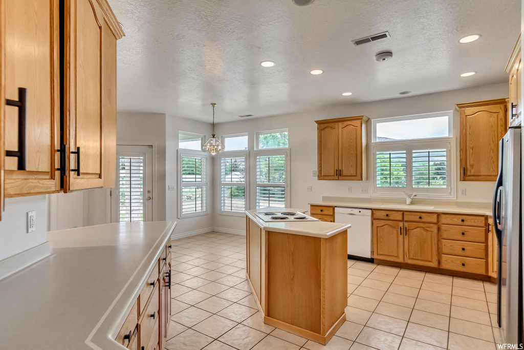 Kitchen with plenty of natural light, electric stovetop, refrigerator, dishwasher, light countertops, light tile floors, and brown cabinets