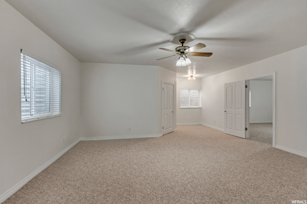 Carpeted spare room featuring a ceiling fan and natural light