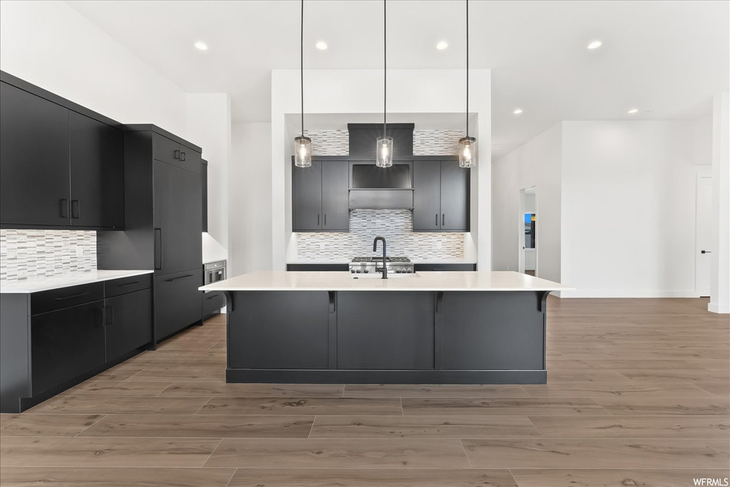 Kitchen with gas cooktop, stainless steel finishes, light countertops, pendant lighting, dark brown cabinets, and light hardwood floors