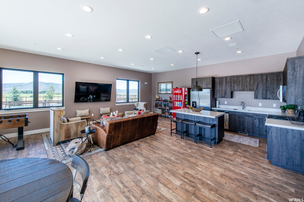 Kitchen with a kitchen breakfast bar, hardwood floors, natural light, microwave, stainless steel refrigerator, TV, light countertops, pendant lighting, and dark brown cabinetry