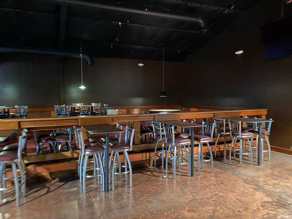 Bar with a kitchen breakfast bar, dark flooring, kitchen island sink, pendant lighting, and dark countertops