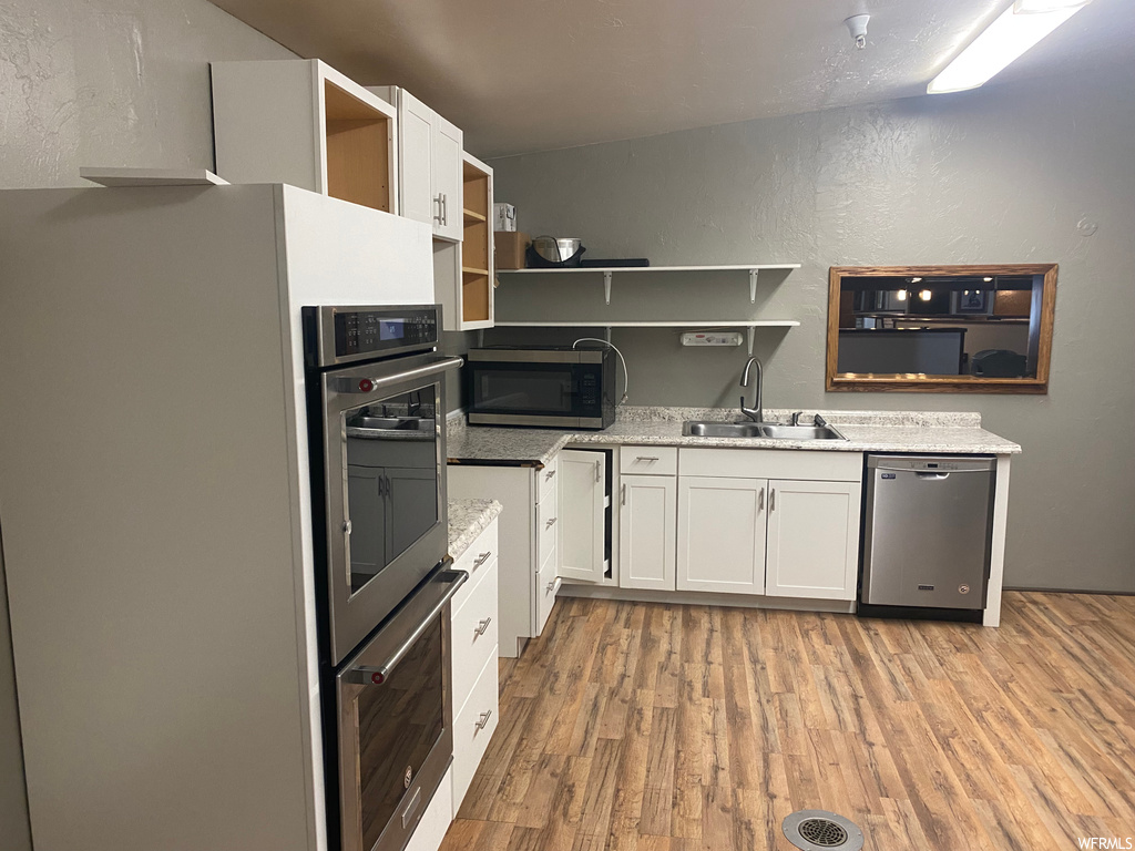 Kitchen featuring dishwasher, oven, refrigerator, microwave, light countertops, light hardwood flooring, and white cabinets