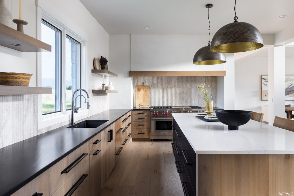 Kitchen with light hardwood flooring, premium range, hanging light fixtures, light countertops, and backsplash