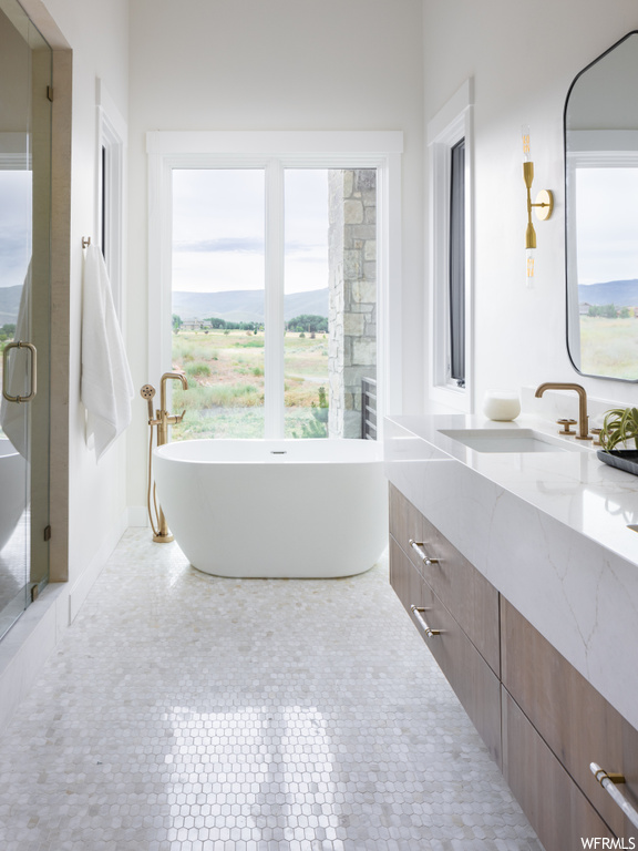 Bathroom featuring light tile floors, a wealth of natural light, a bath, vanity, and mirror