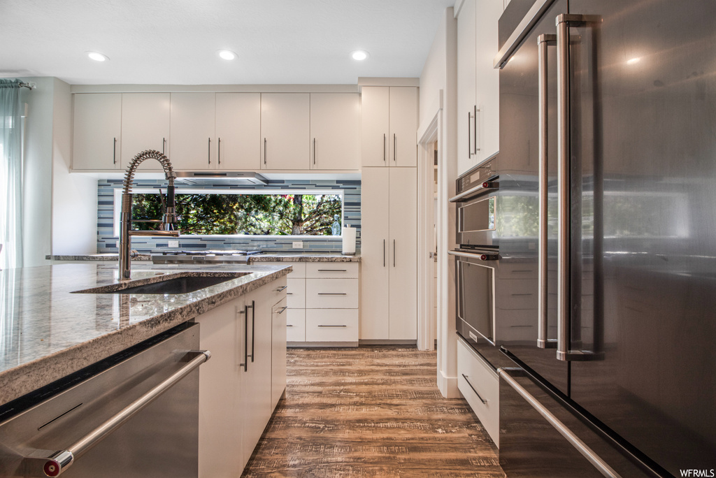 Kitchen featuring refrigerator, dishwasher, double oven, dark hardwood floors, dark granite-like countertops, and white cabinetry