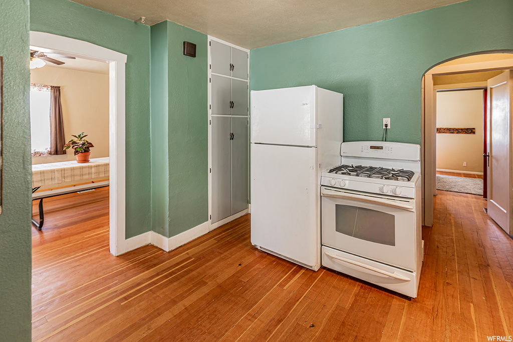 Kitchen featuring a ceiling fan, refrigerator, gas range oven, and light hardwood flooring