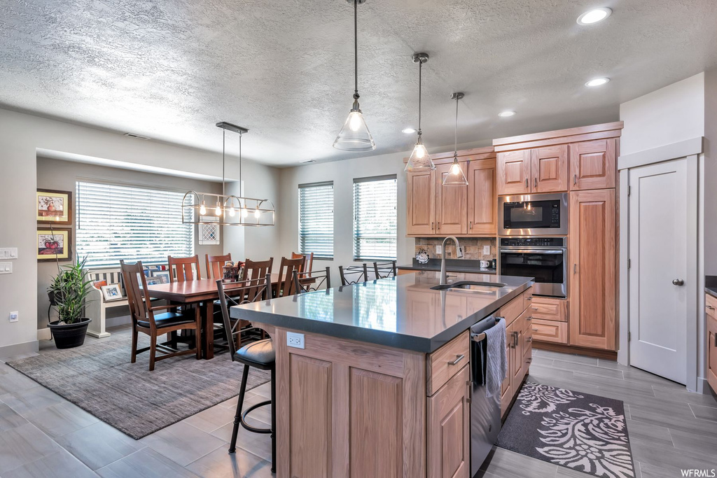 Kitchen featuring a breakfast bar, natural light, dishwasher, oven, light flooring, dark countertops, and pendant lighting