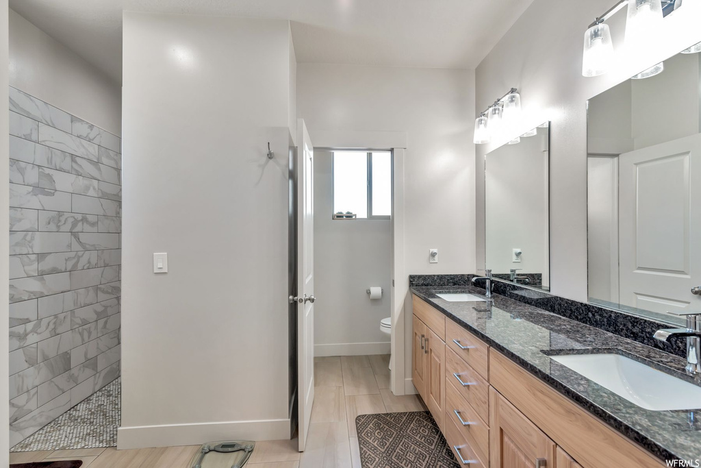Bathroom with hardwood floors, natural light, dual mirrors, a shower, dual vanity, and toilet