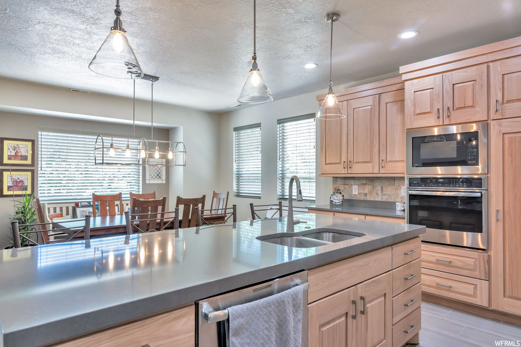 Kitchen featuring natural light, stainless steel dishwasher, oven, microwave, light flooring, and pendant lighting