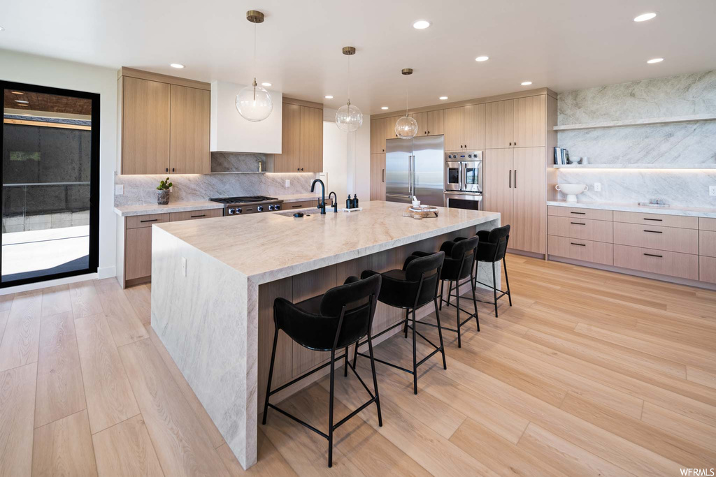 Kitchen featuring a breakfast bar area, gas cooktop, stainless steel appliances, light countertops, an island with sink, light parquet floors, and pendant lighting