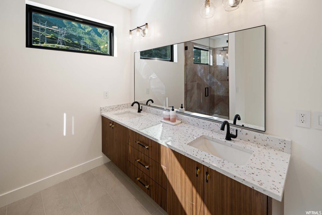 Bathroom featuring tile floors, mirror, dual bowl vanity, and shower with shower door