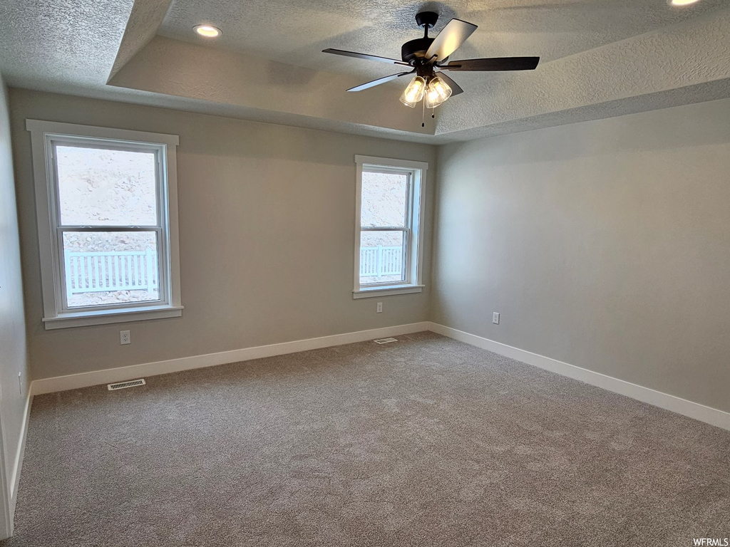Empty room with a tray ceiling, a textured ceiling, carpet, and ceiling fan