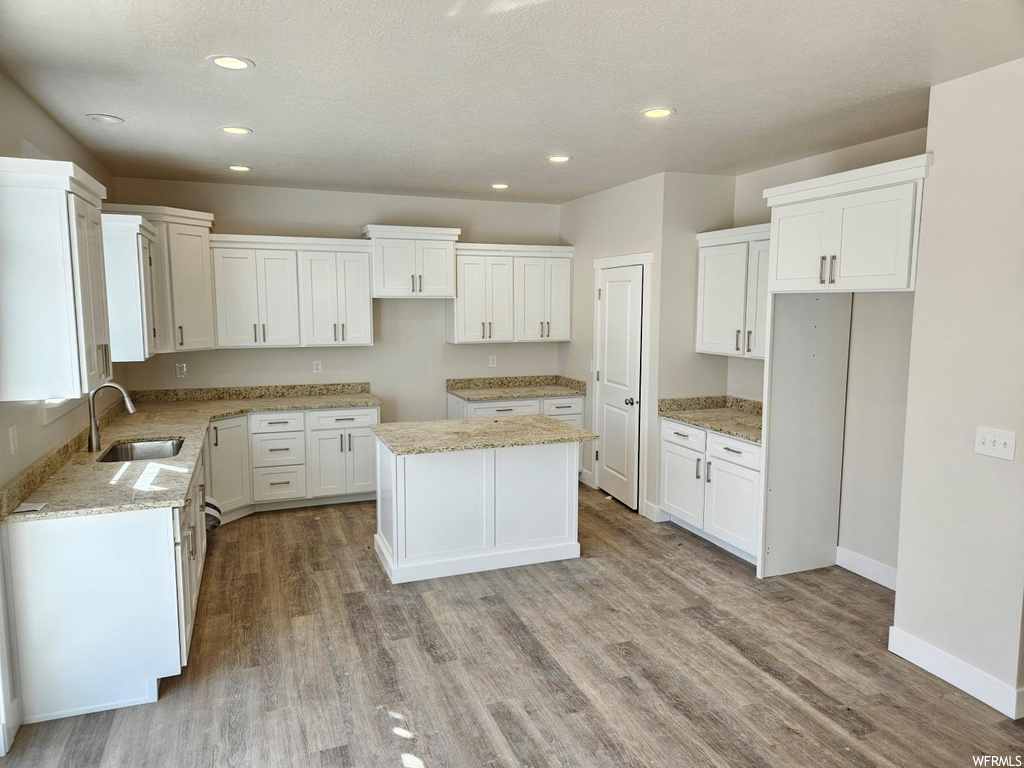 Kitchen featuring wood-type flooring, light stone countertops, and white cabinets