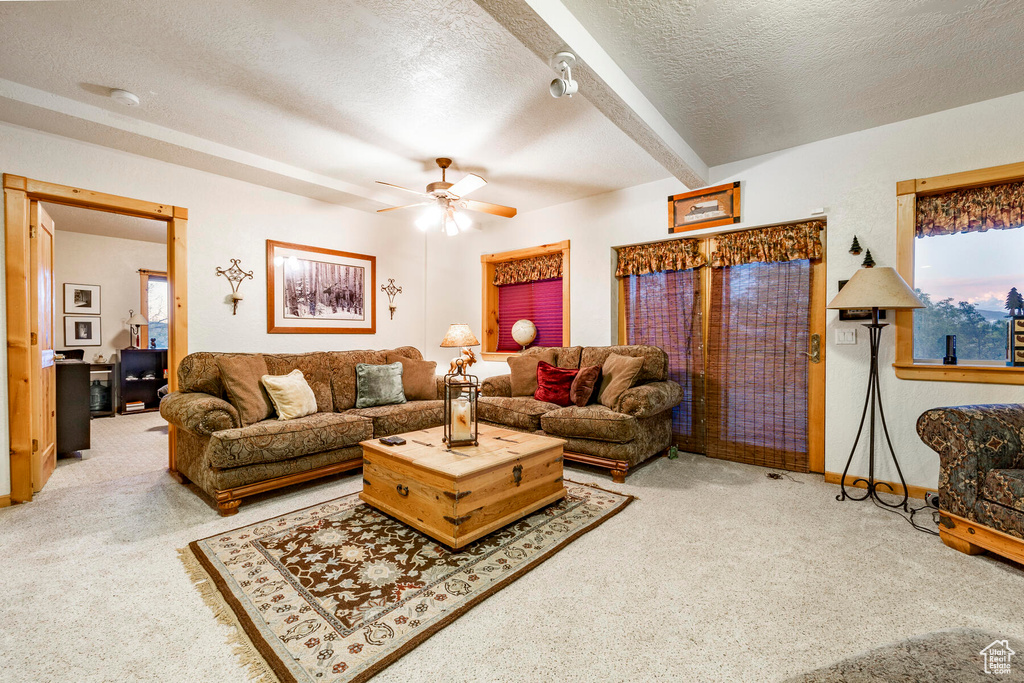 Living room with carpet floors, beamed ceiling, ceiling fan, and a textured ceiling
