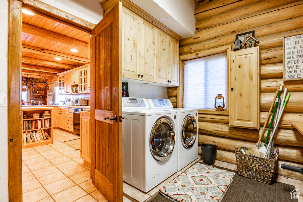 Washroom featuring log walls, light tile flooring, cabinets, and washing machine and clothes dryer
