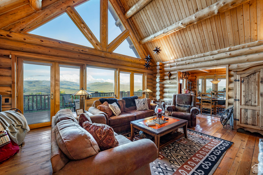 Living room featuring a mountain view, high vaulted ceiling, rustic walls, hardwood / wood-style floors, and beam ceiling