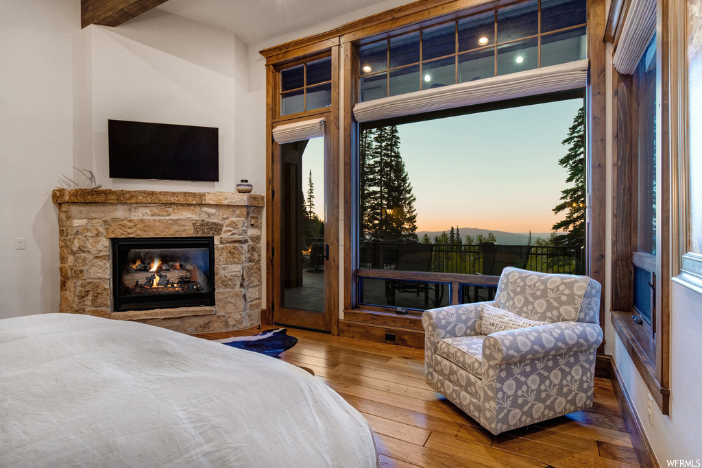 Bedroom featuring multiple windows, hardwood flooring, a fireplace, and beam ceiling