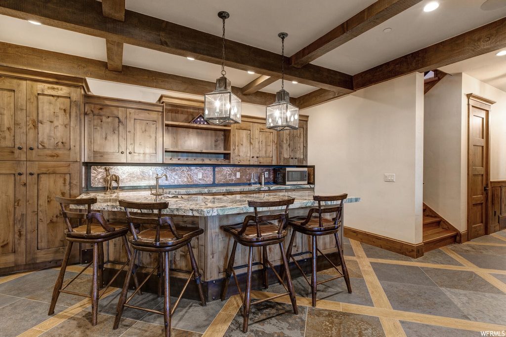 Kitchen featuring backsplash, beamed ceiling, pendant lighting, dark tile floors, and a kitchen breakfast bar