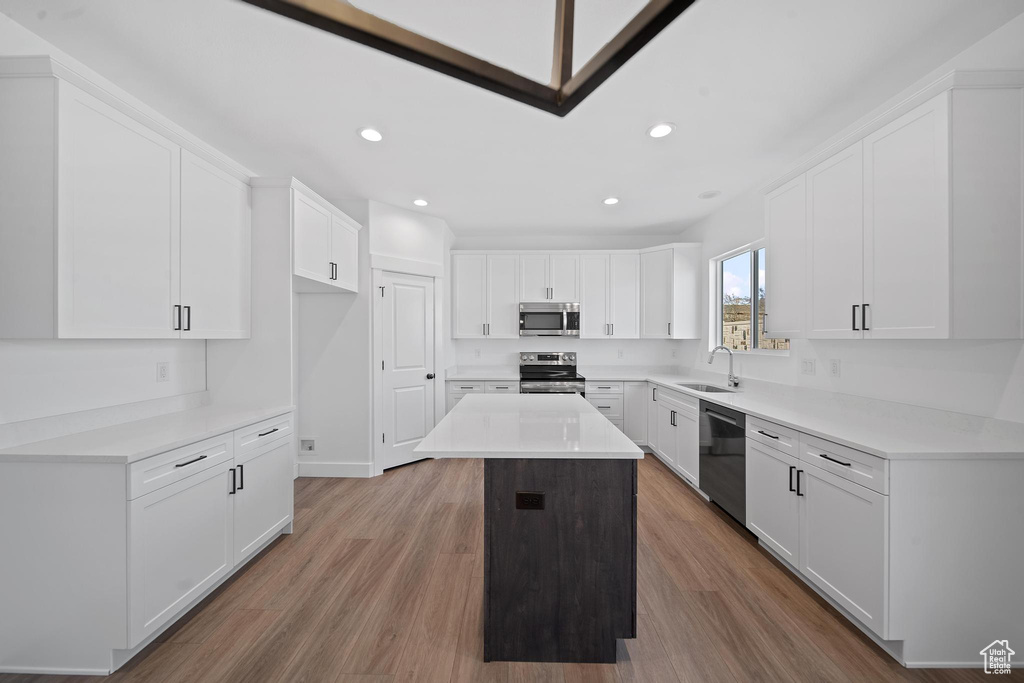 Kitchen with a center island, wood-type flooring, white cabinets, appliances with stainless steel finishes, and sink
