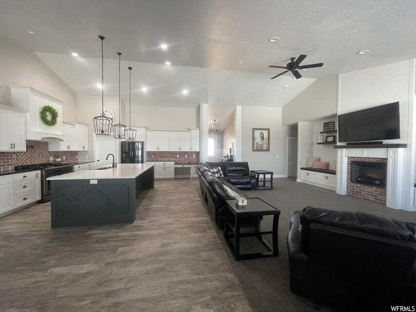 Kitchen featuring a kitchen island, lofted ceiling, a fireplace, a ceiling fan, refrigerator, range oven, TV, white cabinets, and pendant lighting