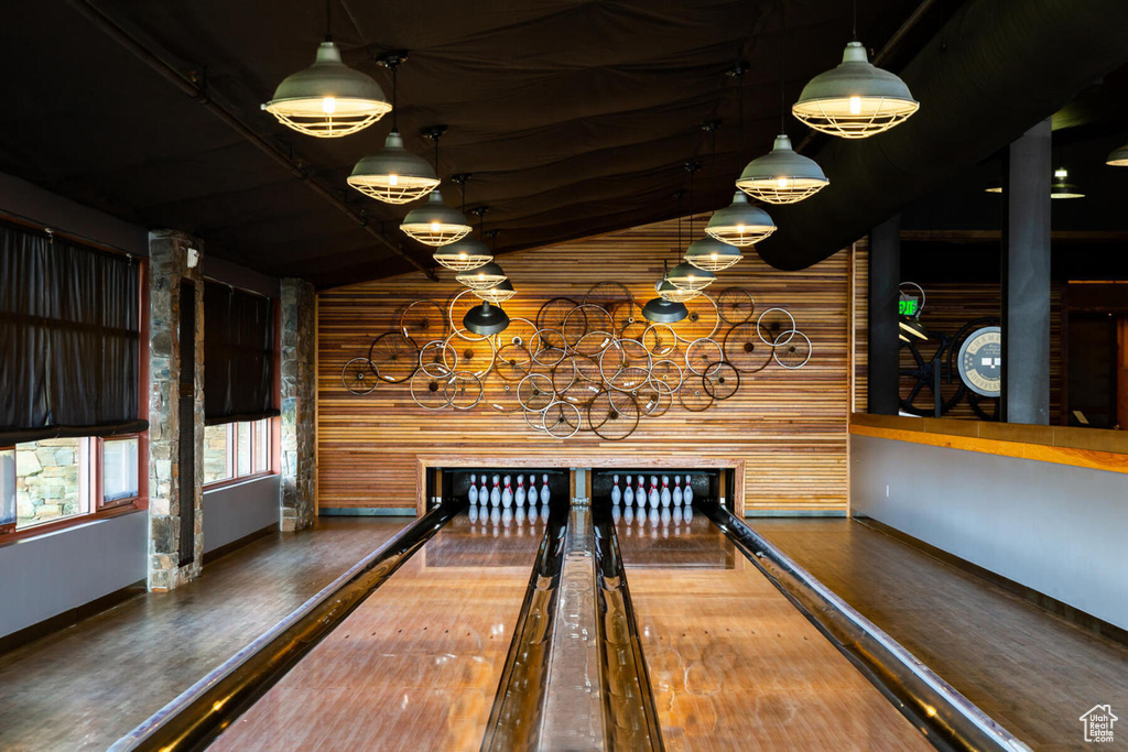 Rec room with lofted ceiling, wood walls, dark wood-type flooring, and a bowling alley