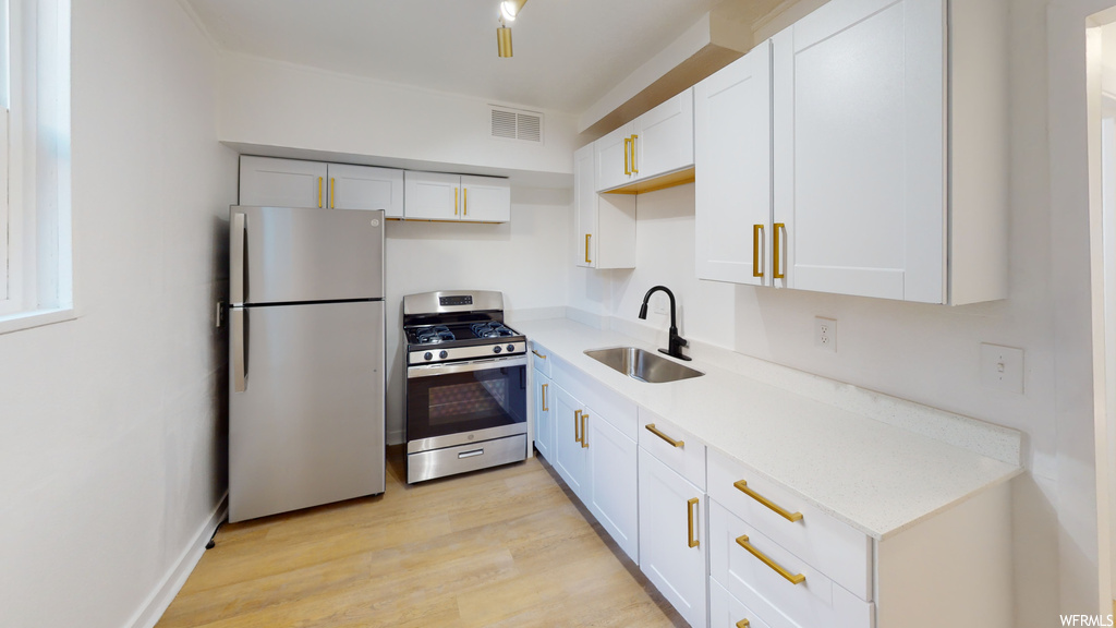 Kitchen featuring refrigerator, gas range oven, light parquet floors, white cabinets, and light countertops