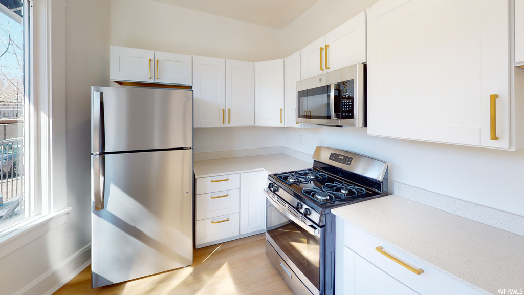 Kitchen with gas range oven, microwave, refrigerator, light countertops, white cabinets, and light hardwood flooring