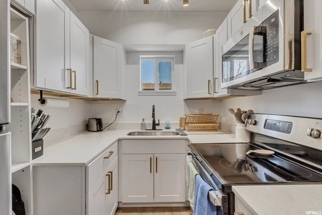 Kitchen featuring microwave, electric range oven, light countertops, and white cabinets
