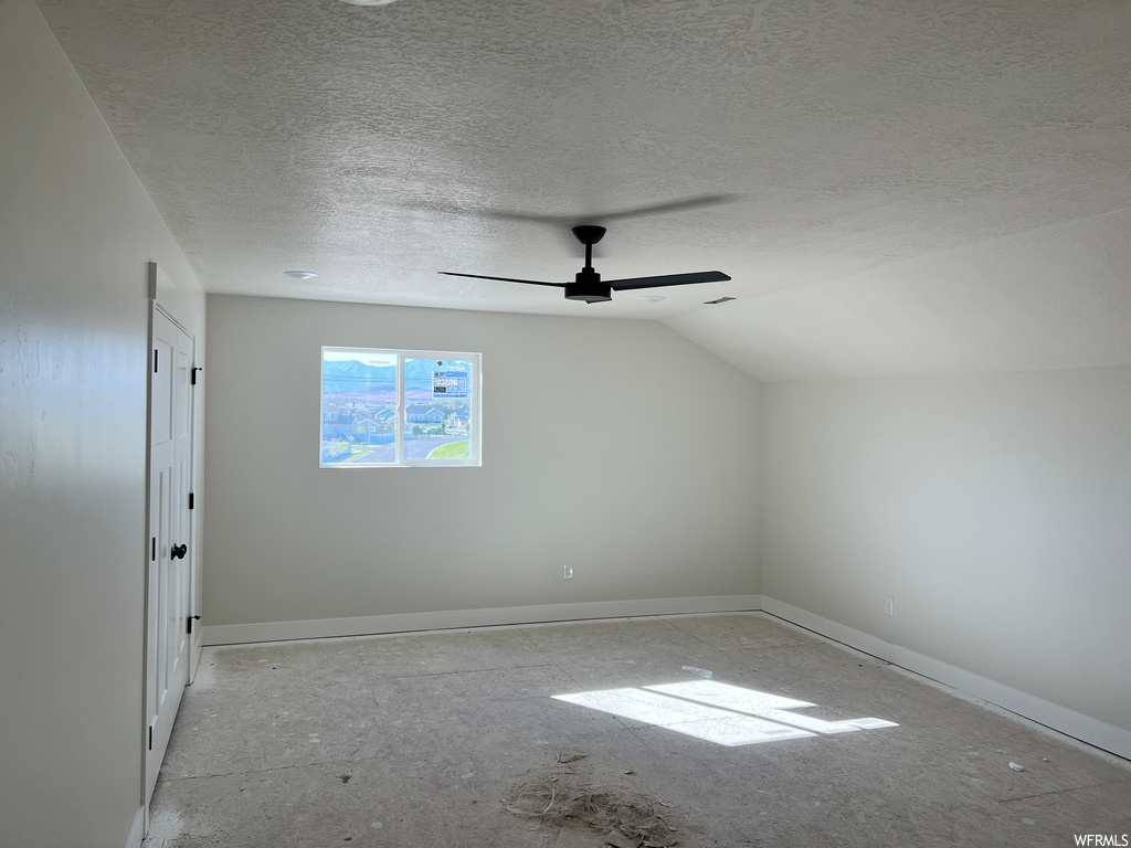 Empty room featuring a textured ceiling, lofted ceiling, and ceiling fan