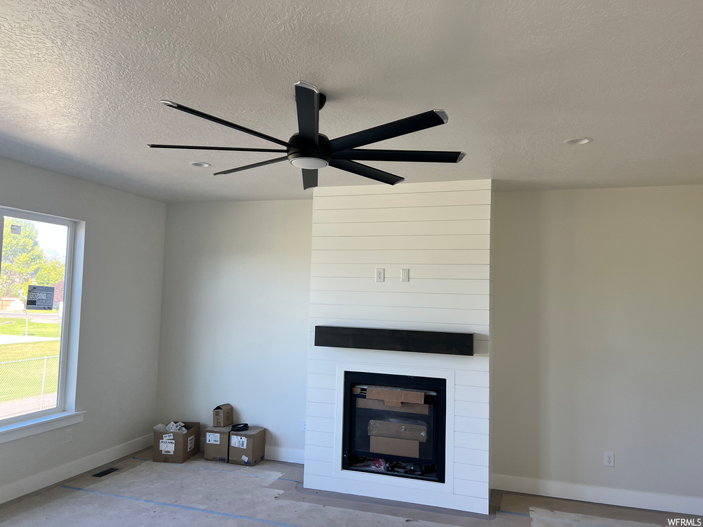 Living room with ceiling fan, a fireplace, and a textured ceiling