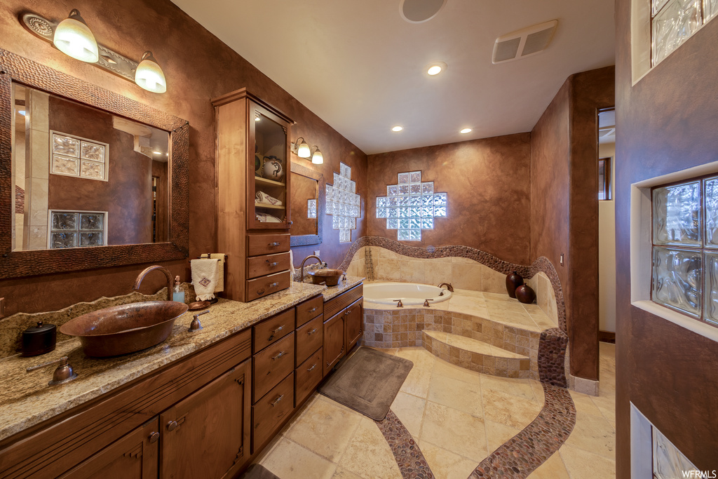 Bathroom with a healthy amount of sunlight, tile flooring, his and hers vanities, mirror, and a bath