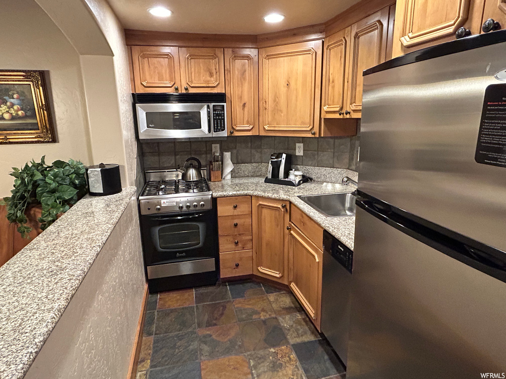 Kitchen with gas range oven, stainless steel appliances, dark tile flooring, light countertops, and brown cabinets