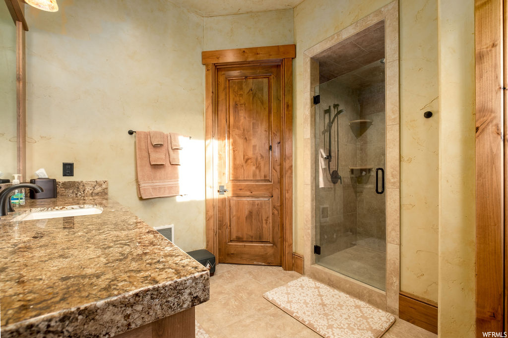 Bathroom with tile flooring, vanity, shower with shower door, and mirror