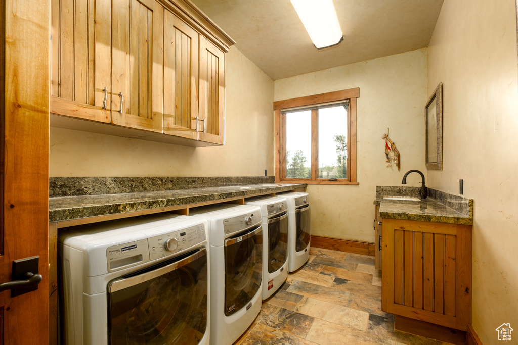 Washroom featuring cabinet space, a sink, stone finish floor, baseboards, and washer and clothes dryer
