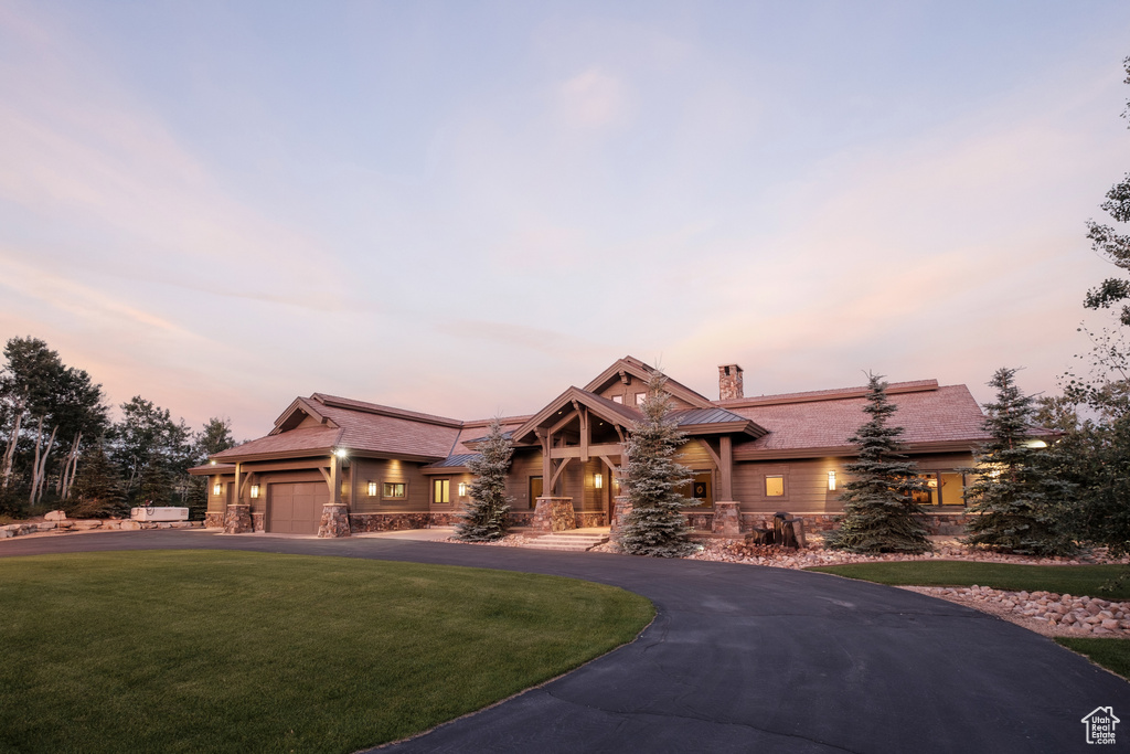 View of front of property featuring a lawn, curved driveway, a chimney, and stone siding