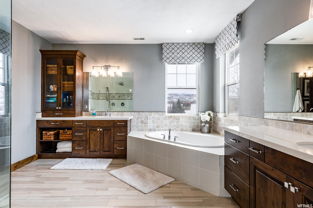 Bathroom with hardwood floors, natural light, double sink vanity, a bath, and multiple mirrors
