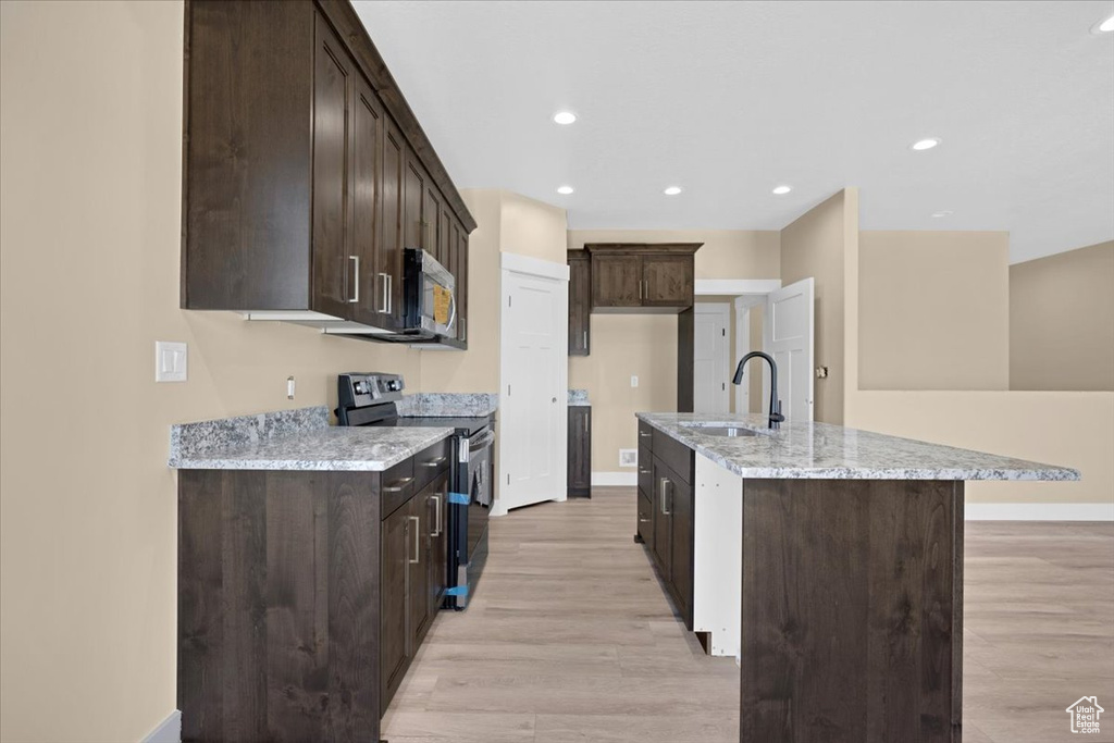 Kitchen featuring dark brown cabinets, light hardwood / wood-style floors, an island with sink, sink, and range with electric cooktop