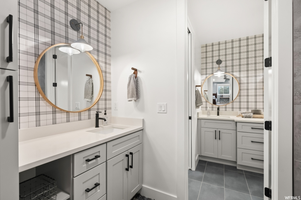 Bathroom with mirror, dark tile flooring, tile walls, and dual bowl vanity