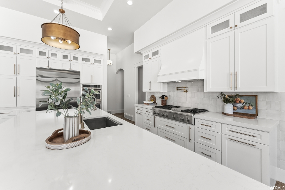 Kitchen with oven, gas stovetop, stainless steel refrigerator, white cabinets, light countertops, and pendant lighting