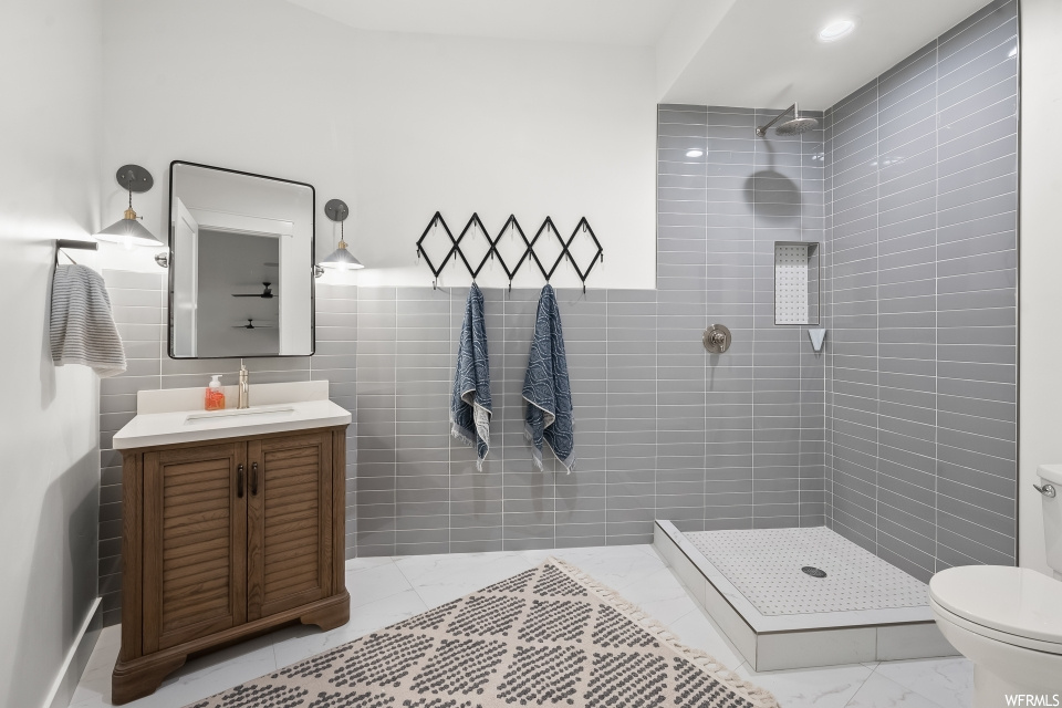 Bathroom featuring tile walls, mirror, tiled shower, large vanity, and light tile floors