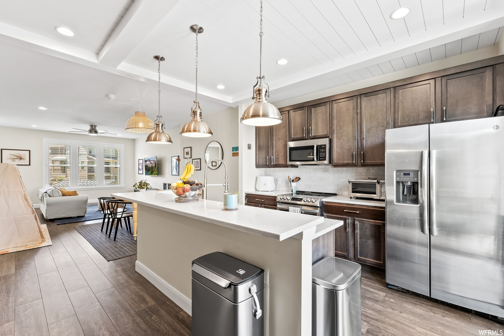 Kitchen with a center island, a kitchen breakfast bar, natural light, range oven, microwave, refrigerator, light parquet floors, light countertops, dark brown cabinetry, and pendant lighting