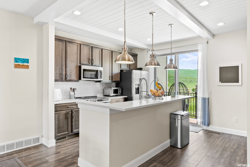 Kitchen with beamed ceiling, a center island, natural light, refrigerator, microwave, light parquet floors, light countertops, and pendant lighting