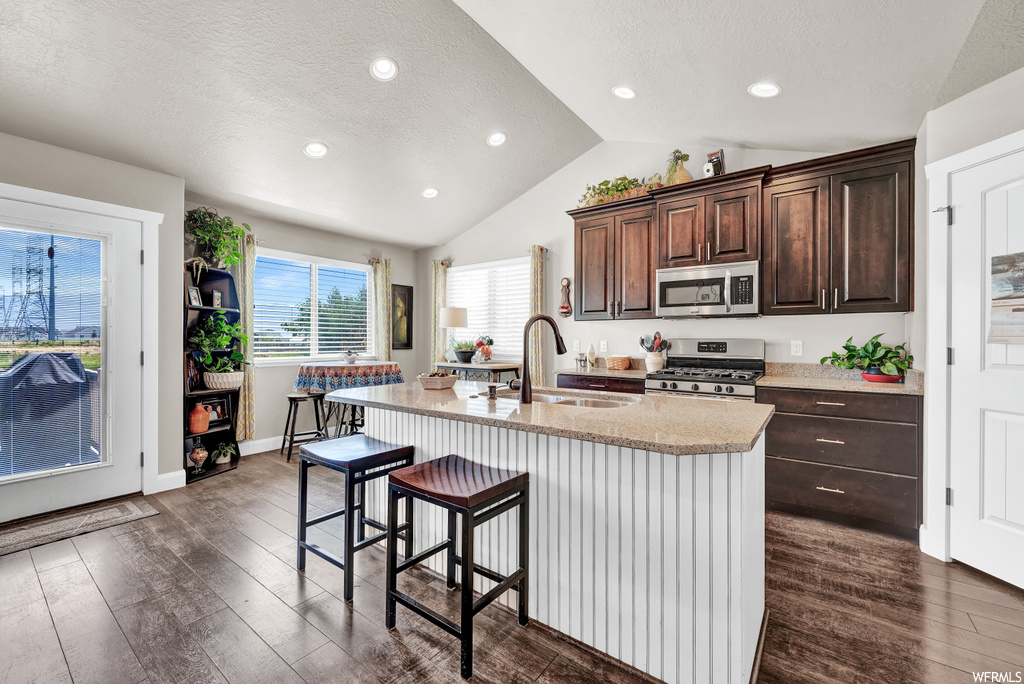 Kitchen with a kitchen breakfast bar, lofted ceiling, plenty of natural light, microwave, gas range oven, light stone countertops, dark hardwood floors, and a kitchen island with sink