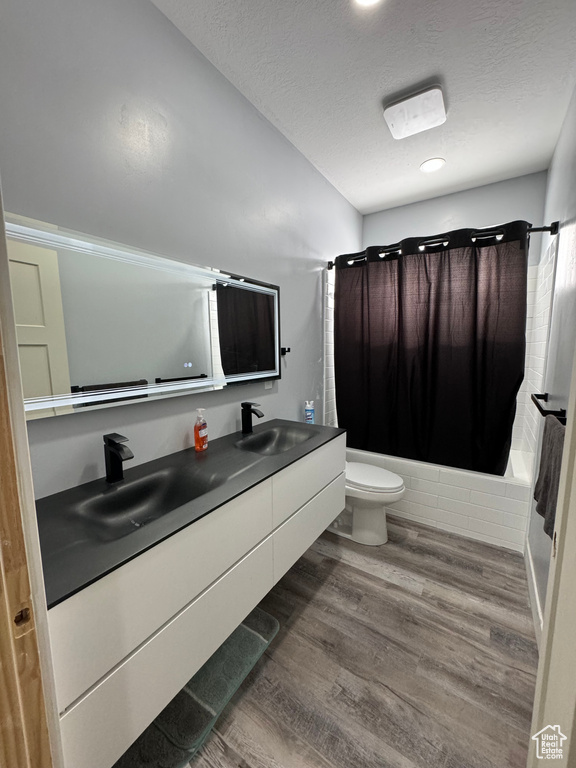 Full bathroom with hardwood / wood-style flooring, toilet, shower / bath combo with shower curtain, and oversized vanity