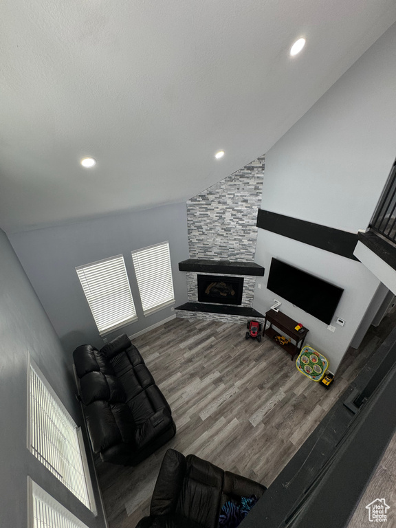 Living room featuring wood-type flooring, a stone fireplace, and lofted ceiling