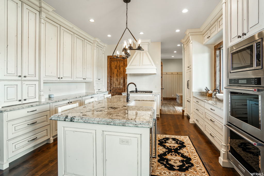 Kitchen featuring a center island, oven, microwave, dark parquet floors, white cabinets, and light granite-like countertops