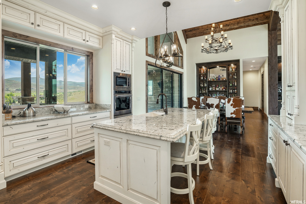 Kitchen with a breakfast bar, natural light, a kitchen island, a chandelier, stainless steel appliances, dark parquet floors, white cabinets, light granite-like countertops, and pendant lighting