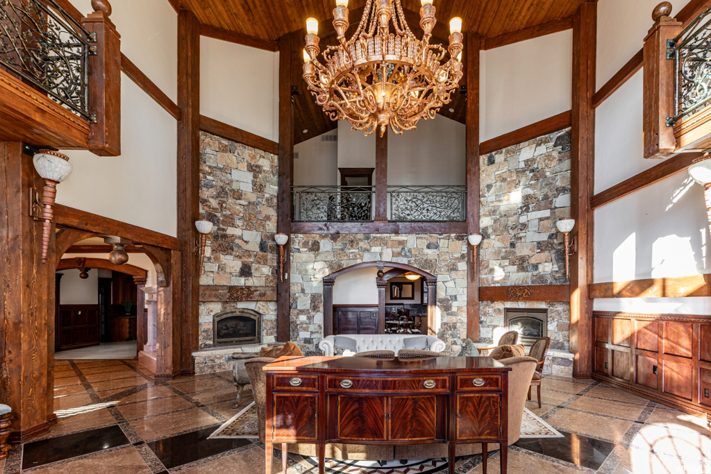 Tiled dining room with wood ceiling, an inviting chandelier, a stone fireplace, and a towering ceiling
